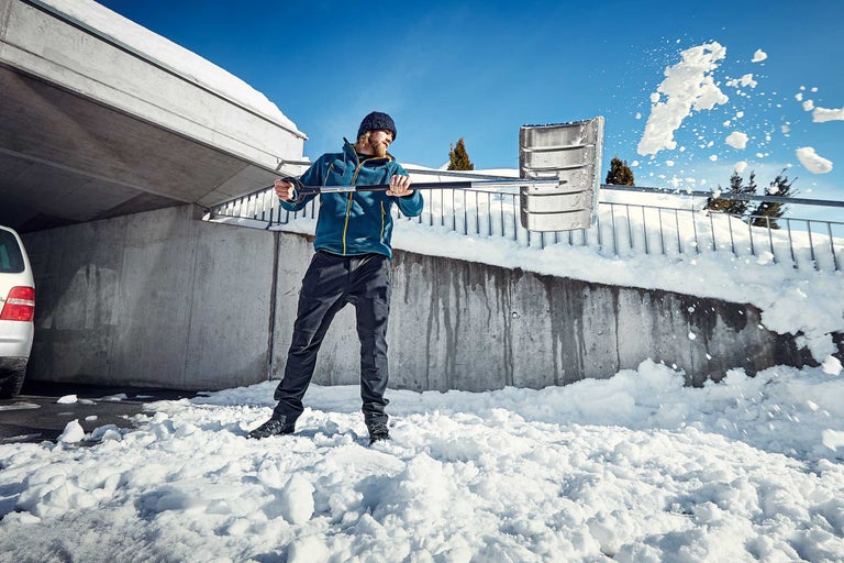 Mann schaufelt Schnee mit einer Schneeschaufel vor einer Betonwand