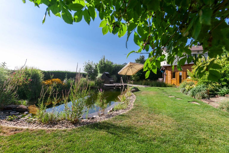Gartenteich mit Bepflanzung und Liegefläche unter einem Sonnenschirm