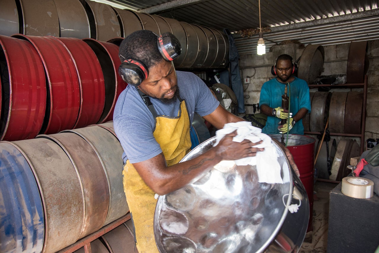 Ein Mann poliert eine Steeldrum in einer Werkstatt, in der mehrere Metallfässer gelagert sind.