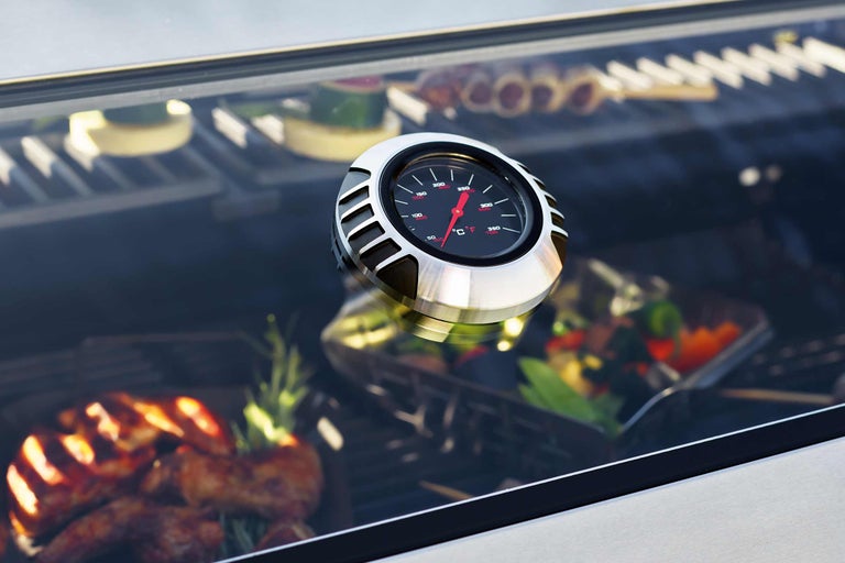 Detailaufnahme eines Grillthermometers mit Speisen im Hintergrund.
