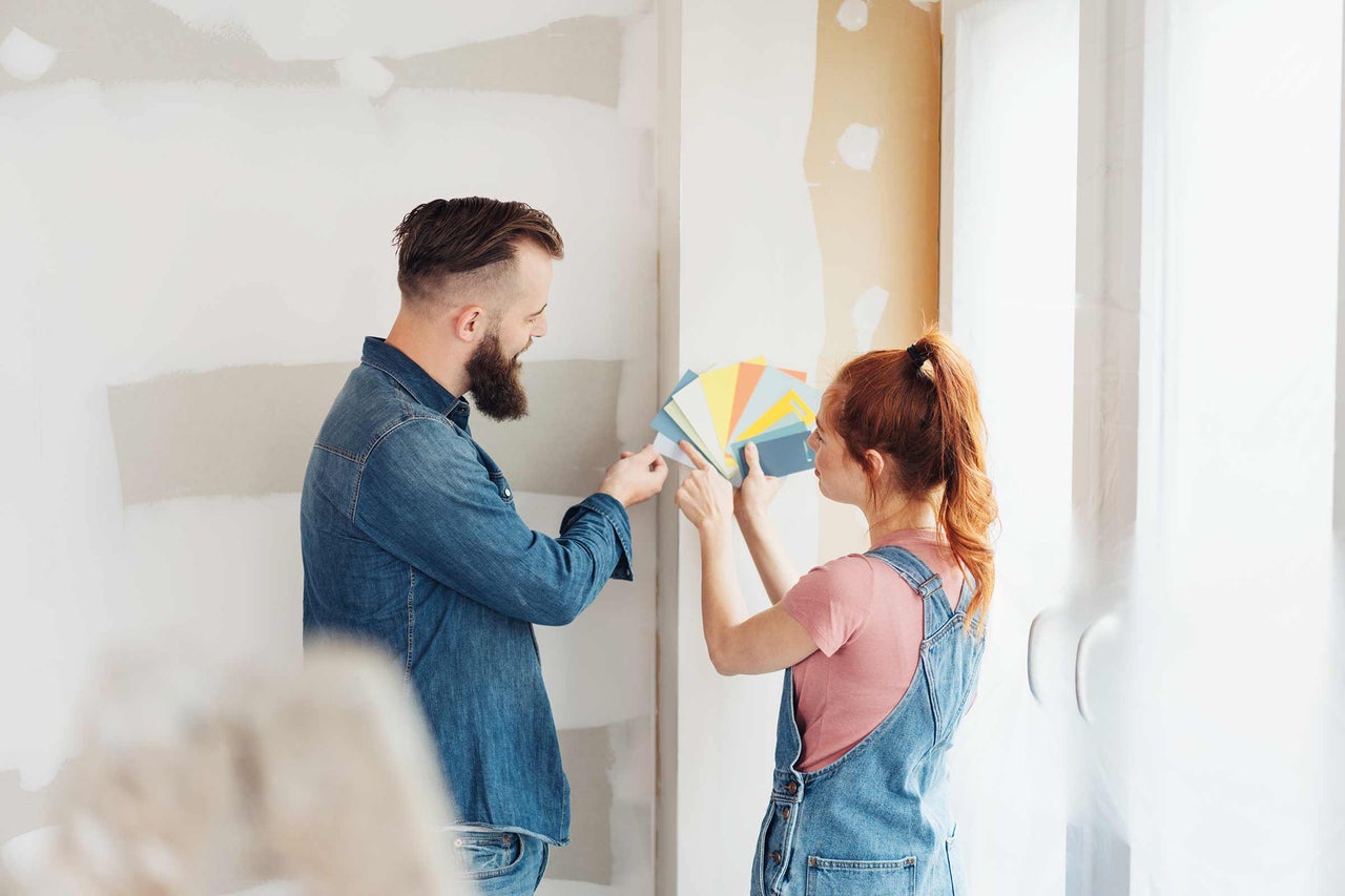 Ein Paar wählt Farbfelder vor einer unfertigen Wand für die Renovierung aus.