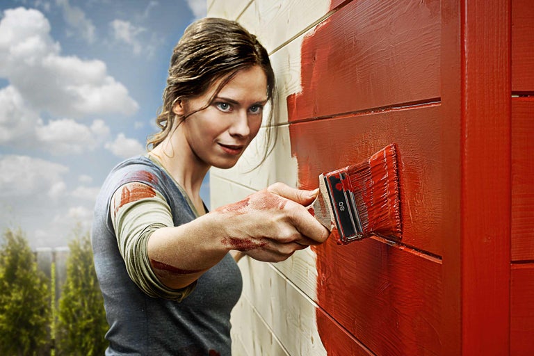 Frau streicht Holzwand mit Pinsel und Holzfarbe