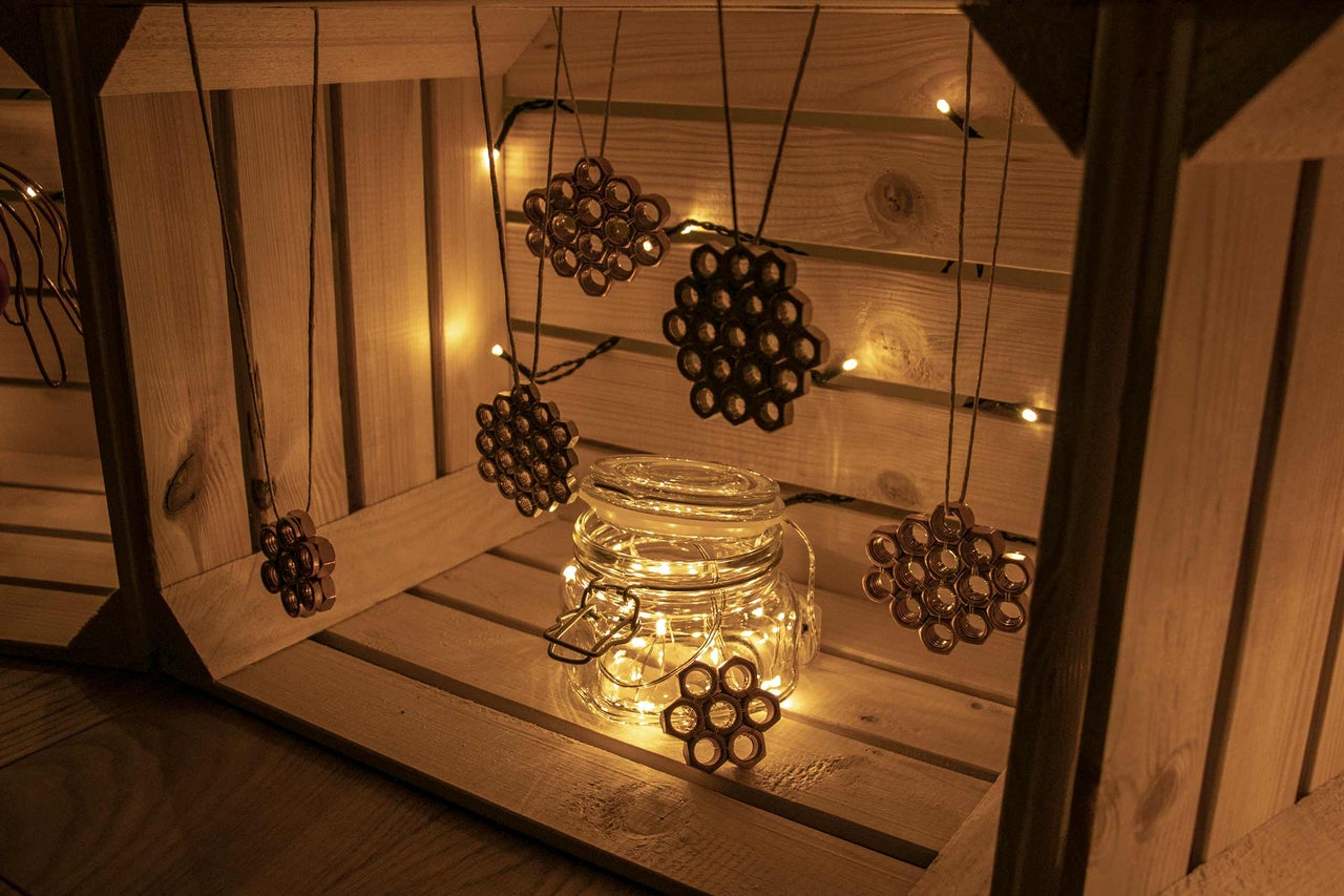 Dekorative Szene mit einem Einmachglas mit Lichterkette und Anhängern aus Muttern in einer Holzkiste.