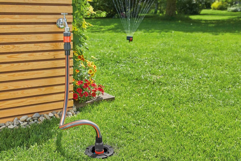 Gartenszene mit Wasserhahn, Schlauchverbinder, Gartenschlauch und Rasensprenger