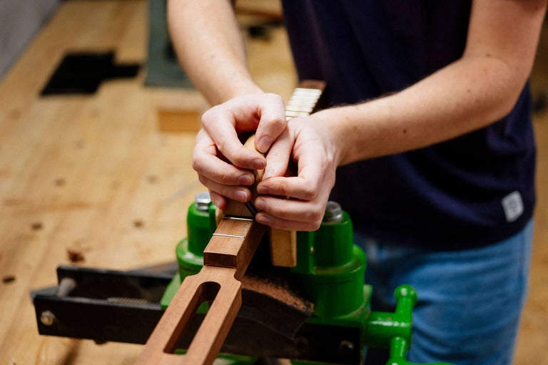 Person arbeitet an einem Gitarrenhals im Schraubstock