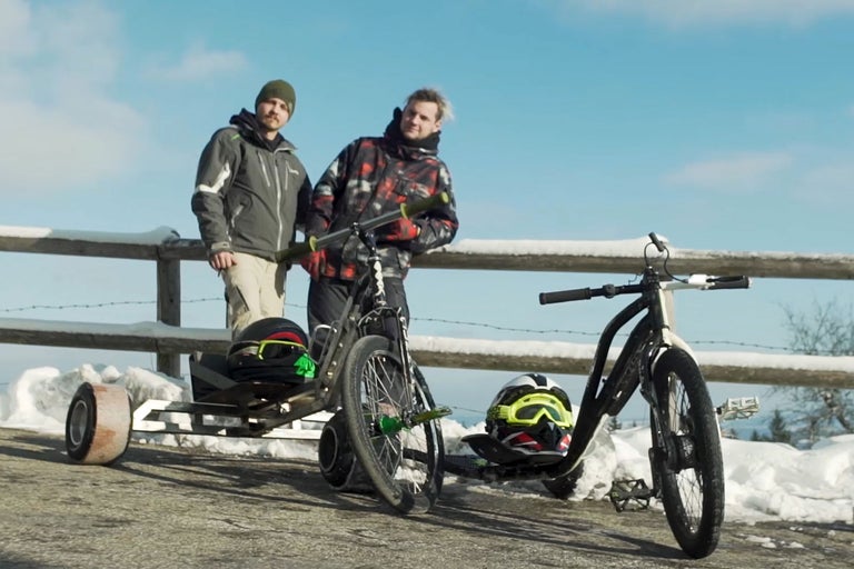 Zwei Männer stehen neben zwei Drifttrikes im Schnee.