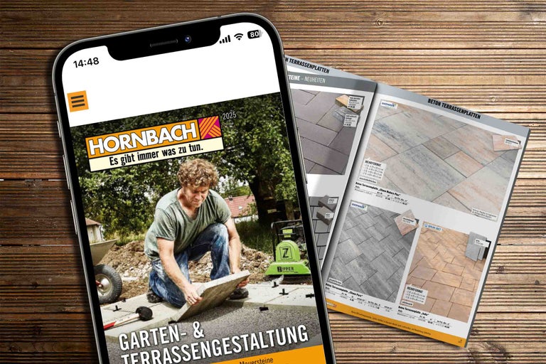Smartphone mit der geöffneten Hornbach Webseite und ein Katalog für Terrassenplatten auf einem Holzboden.