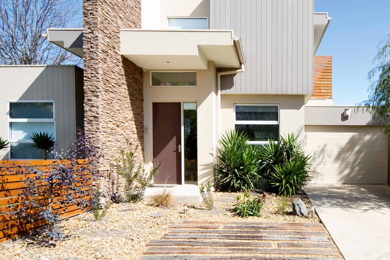 Außenansicht eines modernen Hauses mit Steinfassade, Holzzaun und Gartenlandschaft