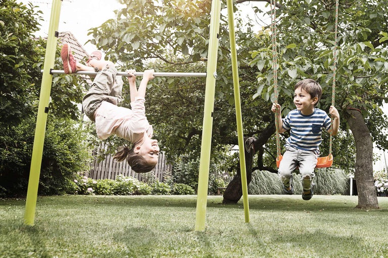Kinder spielen auf einer Schaukel und einer Reckstange im Garten.