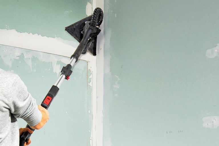 Eine Person schleift mit einem Schleifgerät eine Gipskartonwand.