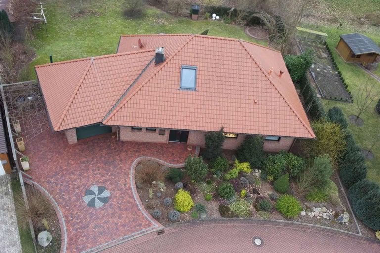 Luftaufnahme eines Hauses mit Ziegeldach, gepflasterter Einfahrt und Garten