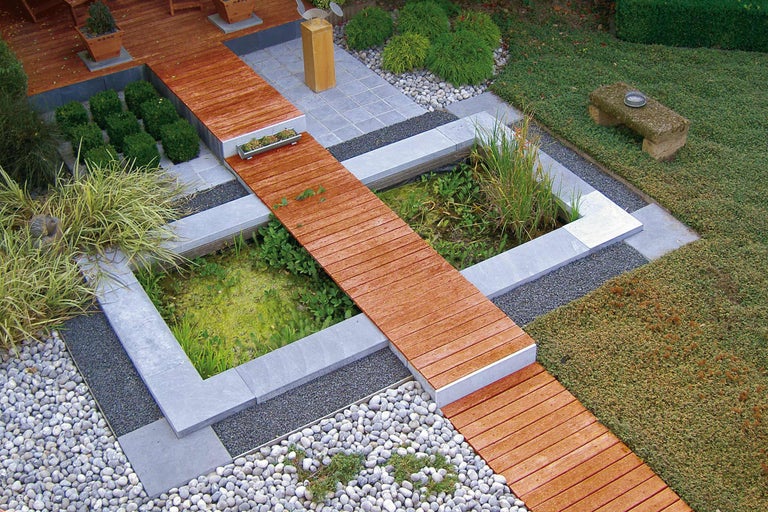 Ansicht eines Gartenteichs mit Holzsteg, umgeben von Steinen und Pflanzen
