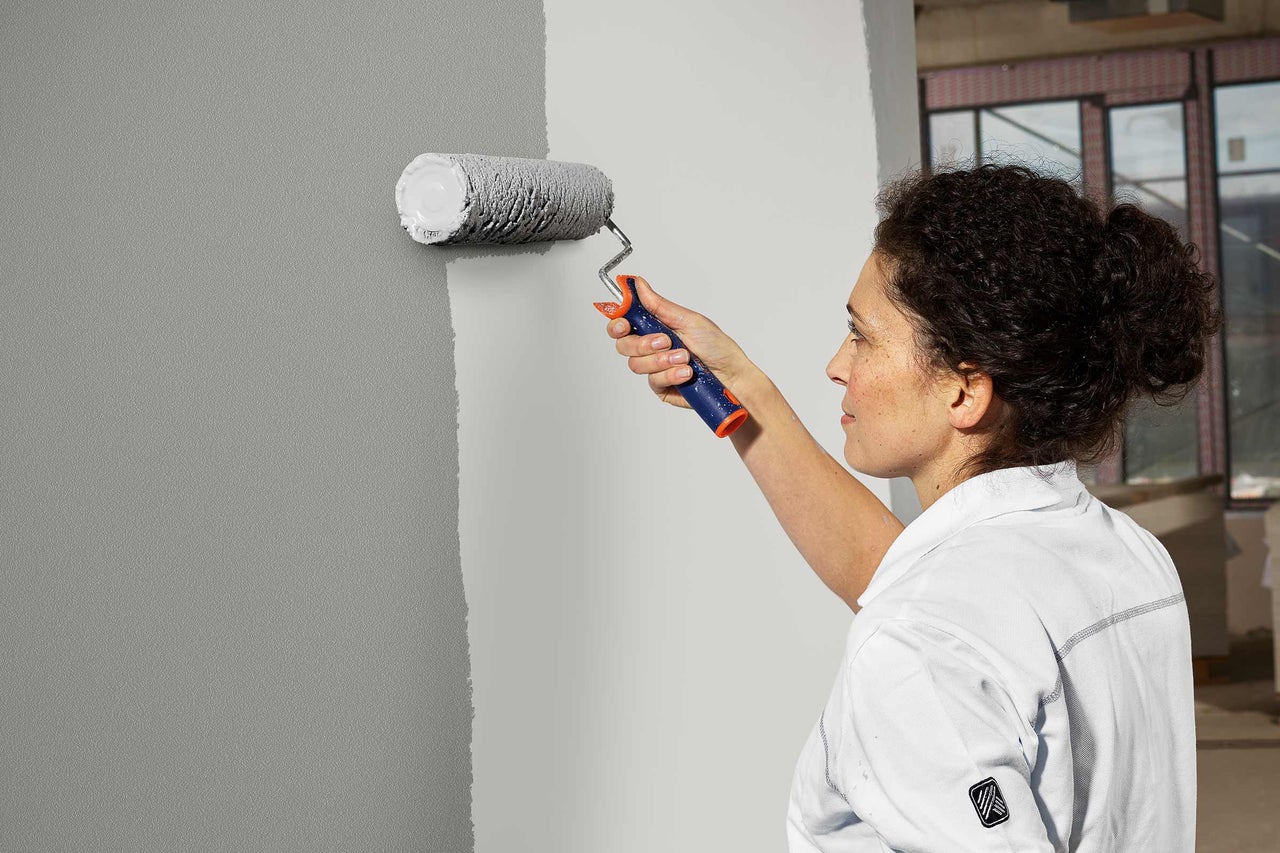Frau streicht Wand mit Farbroller grau
