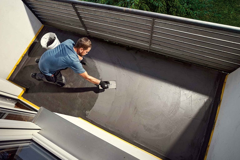 Ein Mann trägt eine graue Beschichtung mit einer Glättkelle auf einen Balkon auf