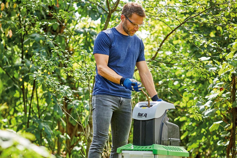 Mann bedient einen Häcksler im Garten.