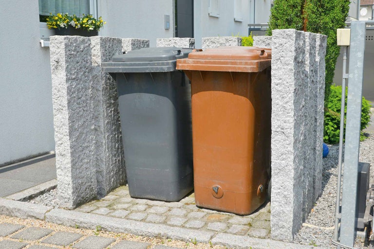 Zwei Mülltonnen in einer Mülltonnenbox aus Stein