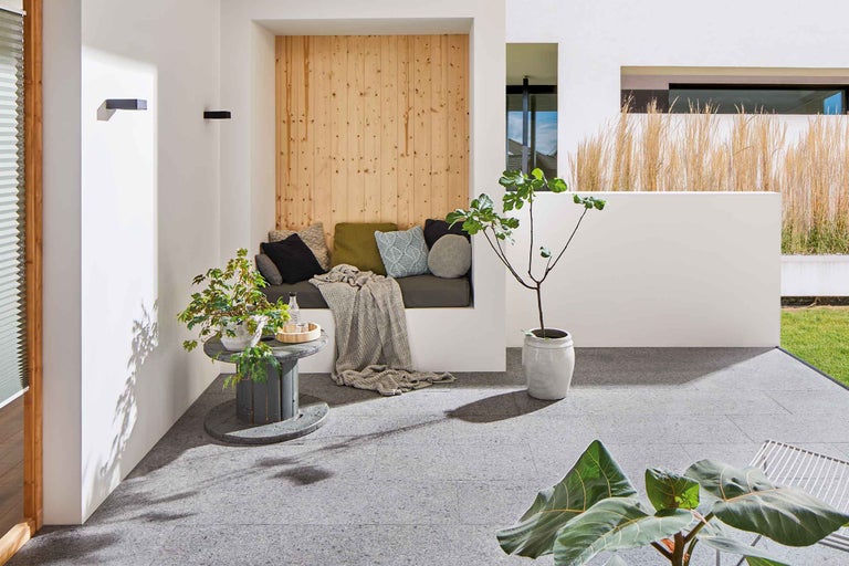 Modern gestalteter Außenbereich mit Sitzbereich, Pflanzen und Bodenplatten.