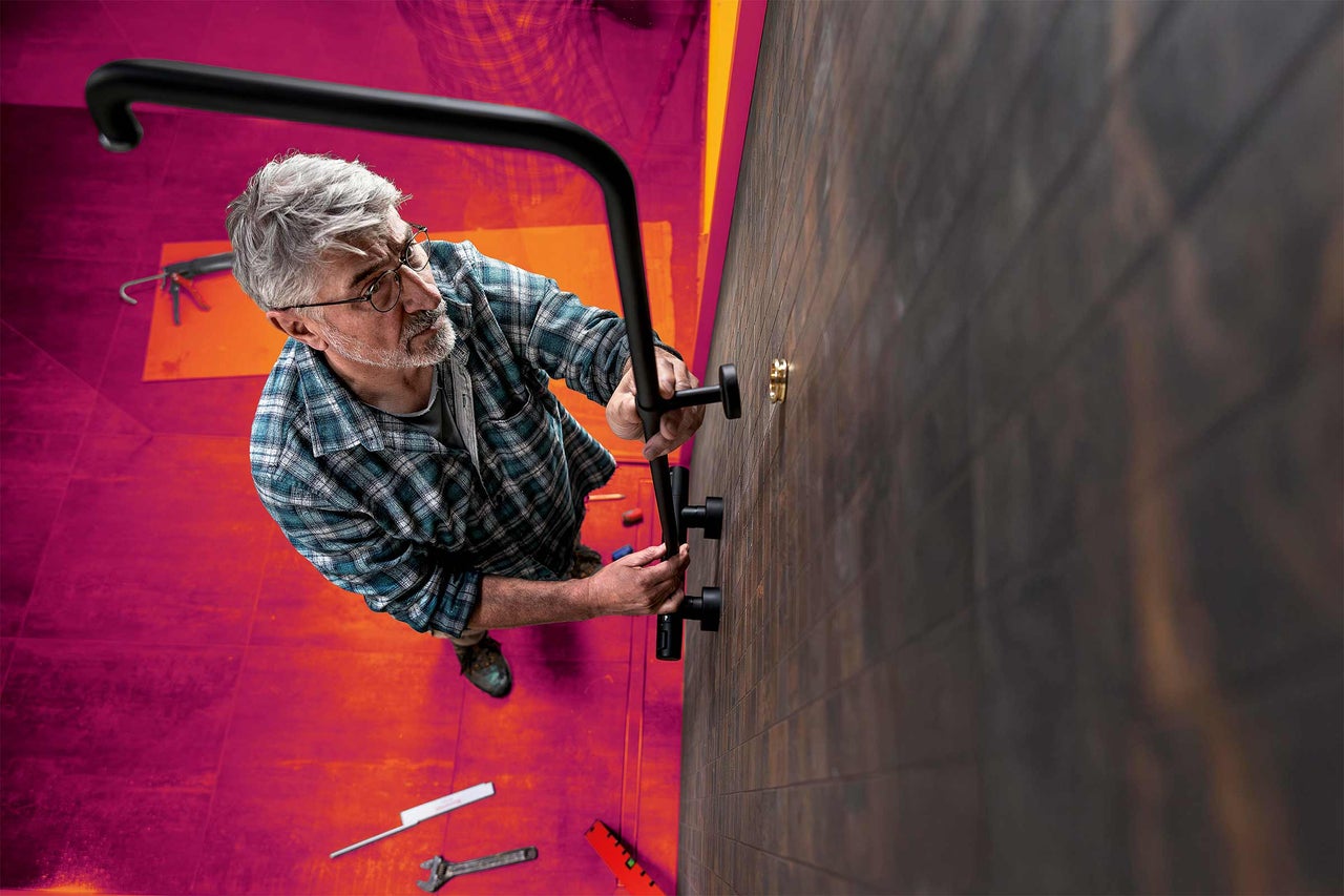 Ein Handwerker montiert eine Duschstange an einer gefliesten Wand.