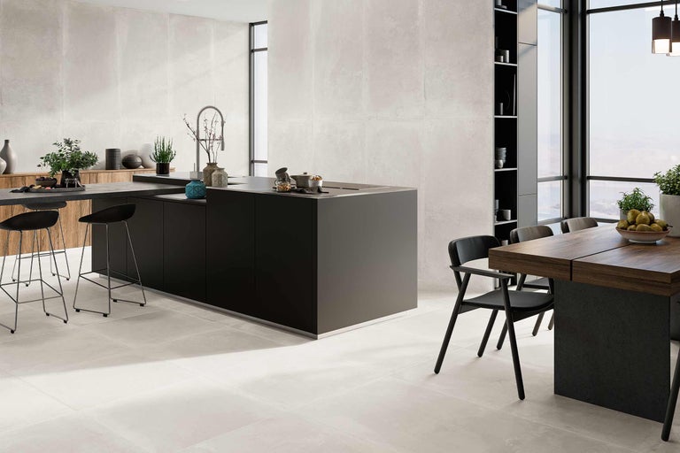 Heller Raum mit großformatigen Fliesen an Boden und Wand, einer Kücheninsel und einem Esstisch.