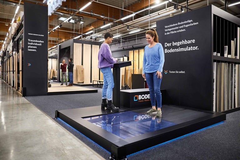 Frauen nutzen den Bodensimulator im Hornbach Markt, um verschiedene Bodenbeläge auszuprobieren.