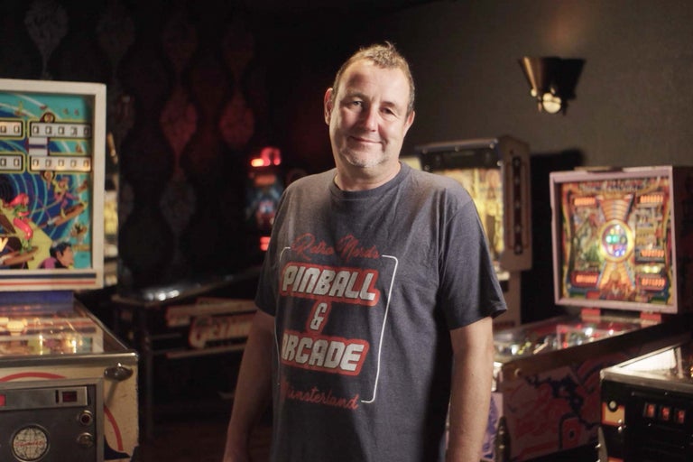 Ein Mann steht in einem Raum mit mehreren Flipperautomaten.