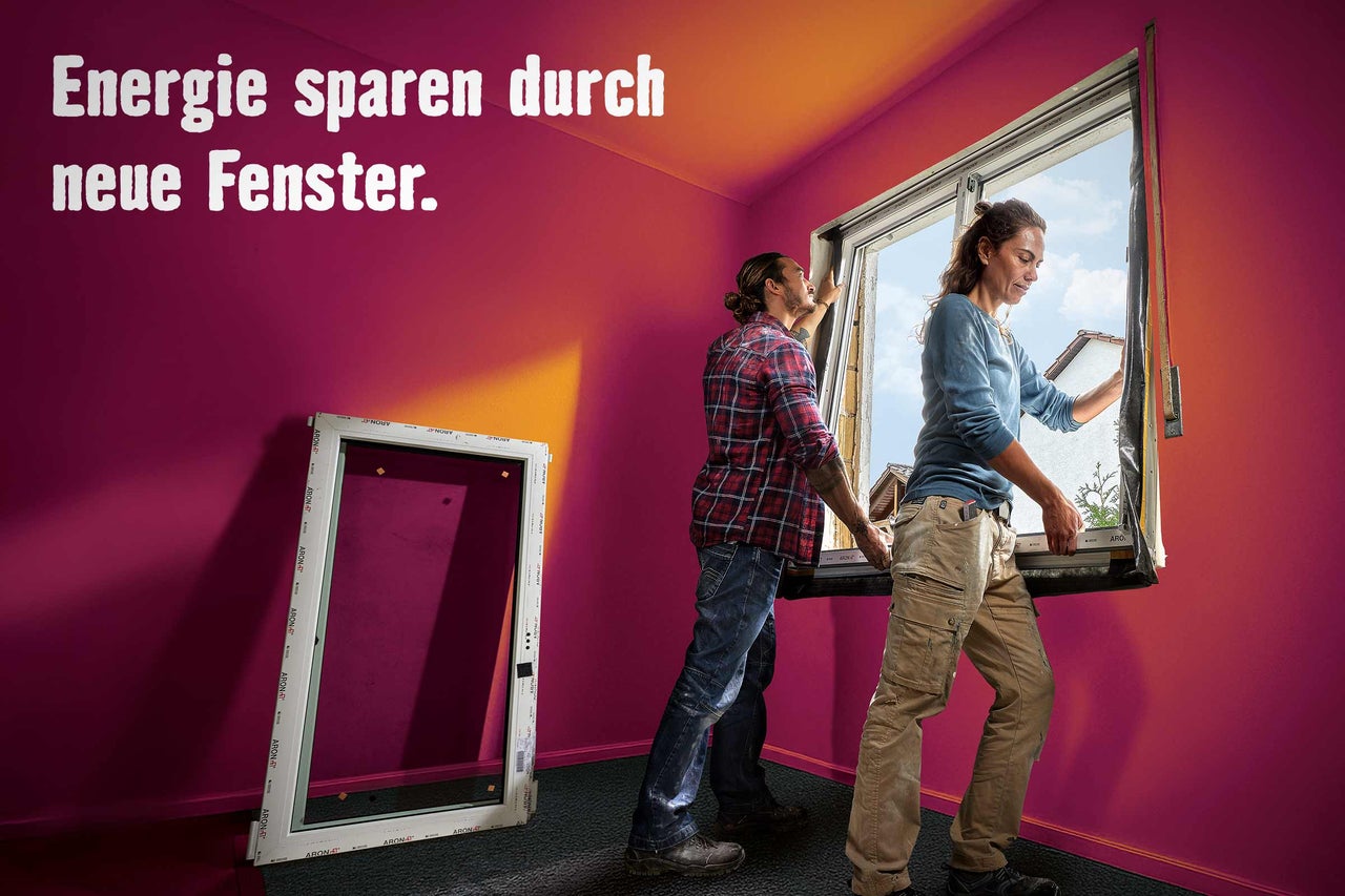 Zwei Personen installieren ein neues Fenster in einem renovierten Raum, um Energie zu sparen.