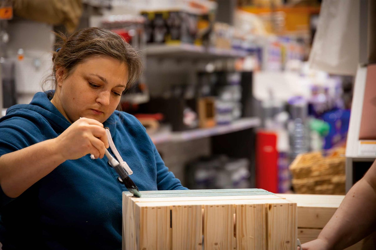 Frau bemalt Holzkiste mit Pinsel