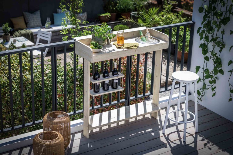 Holzbartisch mit Flaschenhalter und Hocker auf einem Balkon mit Pflanzen
