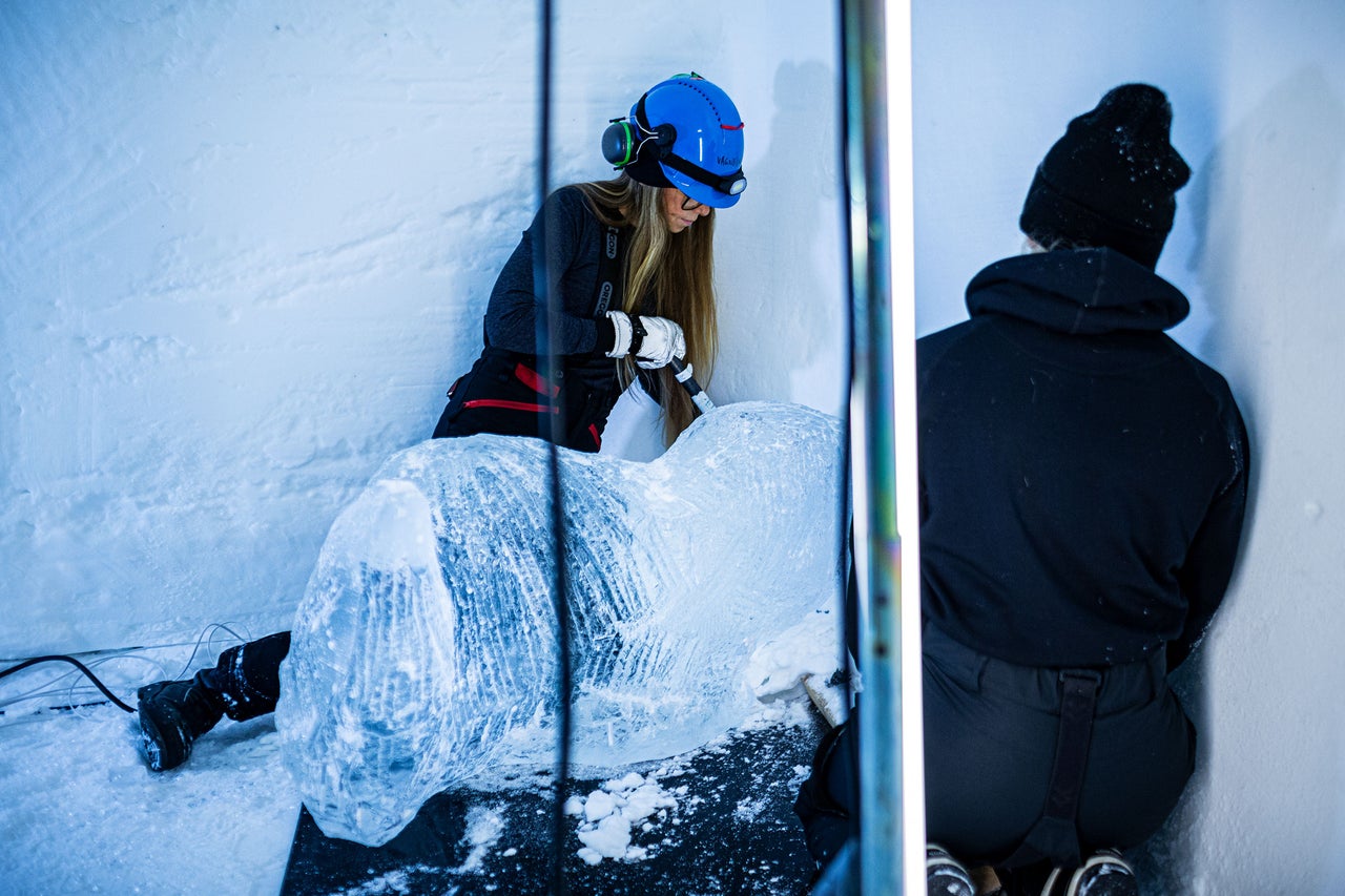 Eisbildhauerin bei der Arbeit an einer Eisskulptur mit Werkzeug und Schutzkleidung.
