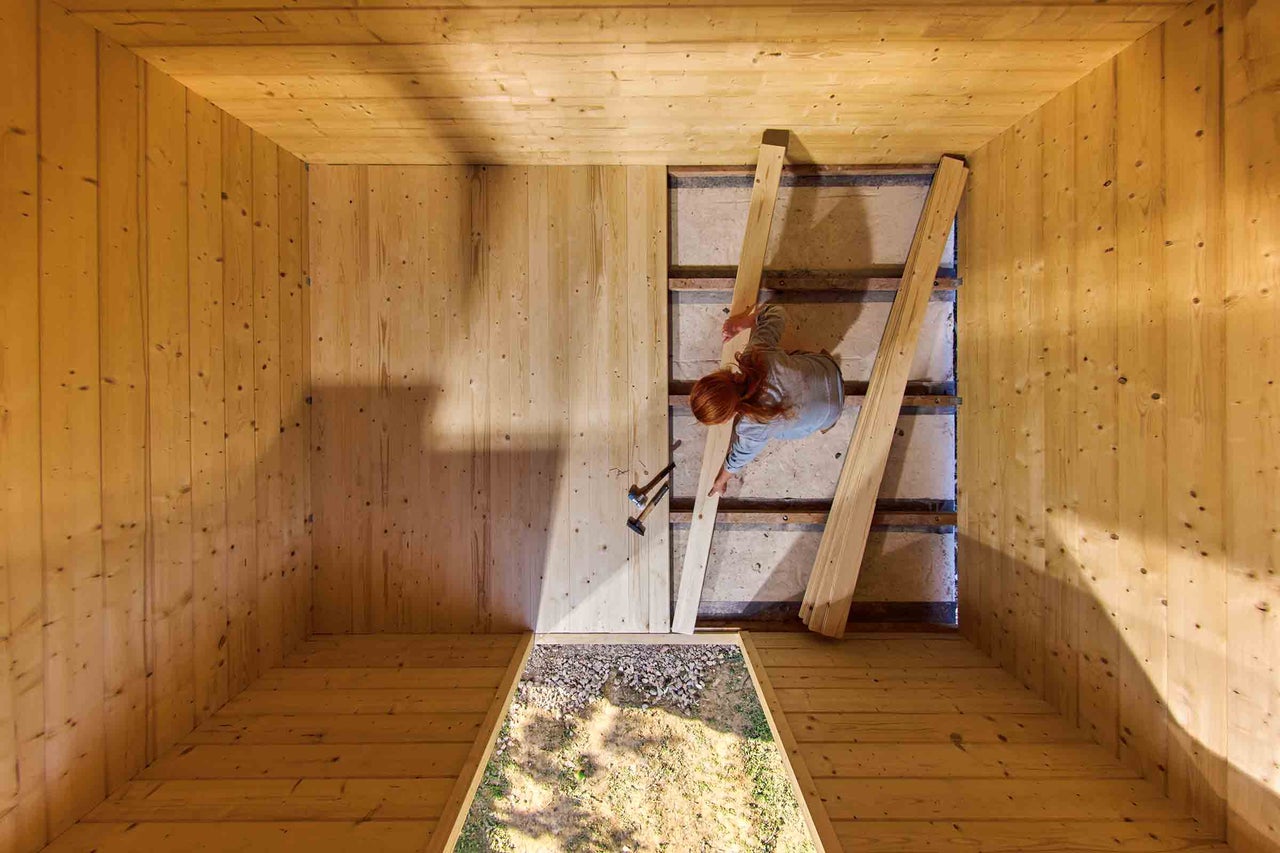 Innenansicht eines Holzhauses mit einer Frau, die Holzboden verlegt.