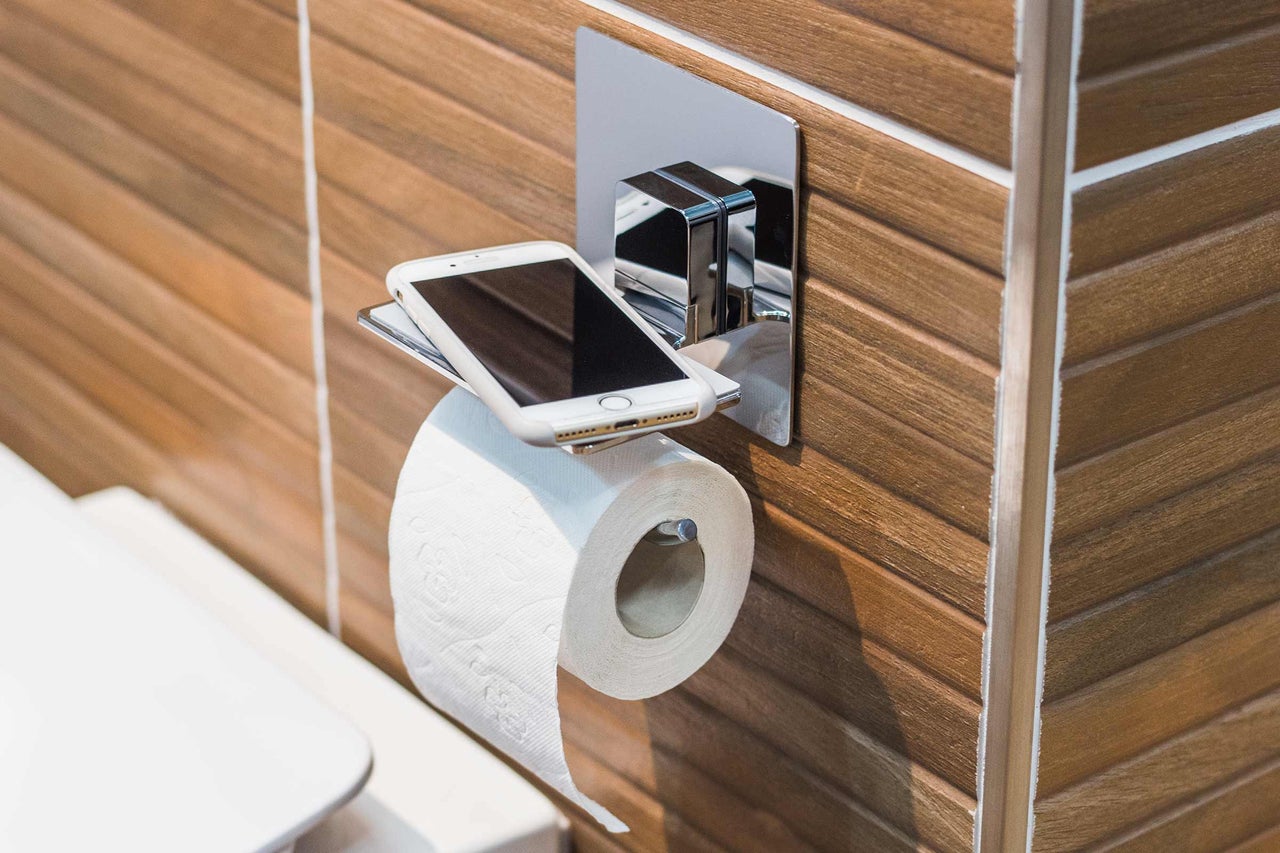 Toilettenpapierhalter mit Ablage und Mobiltelefon im Badezimmer.