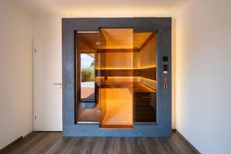 Moderne Innensauna mit Glasfront und Glastür, Innenausbau aus Holz mit Saunabänken und indirekter LED-Beleuchtung.