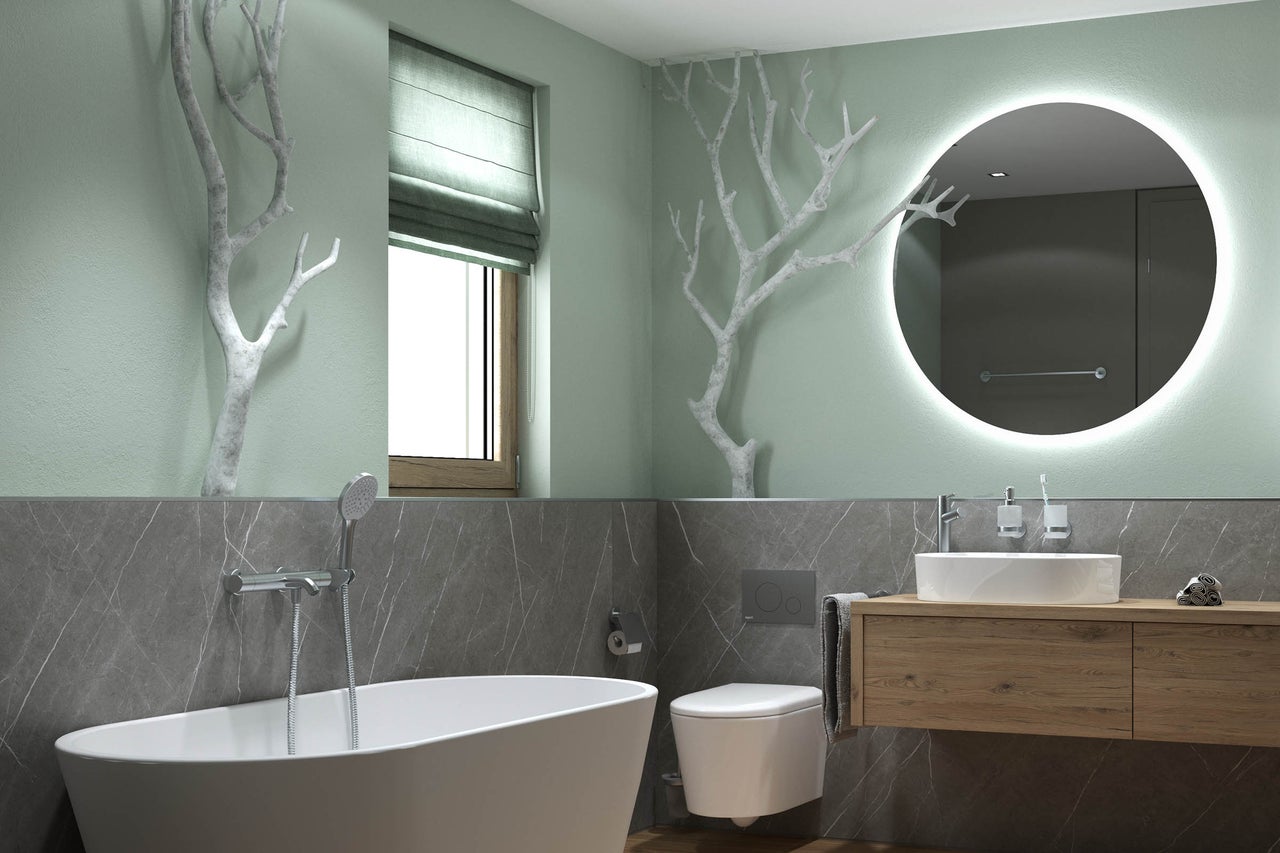 Modernes Badezimmer mit freistehender Badewanne, wandhängender Toilette und Holz-Waschtisch. Ein großer runder beleuchteter Spiegel und dekorative Äste.