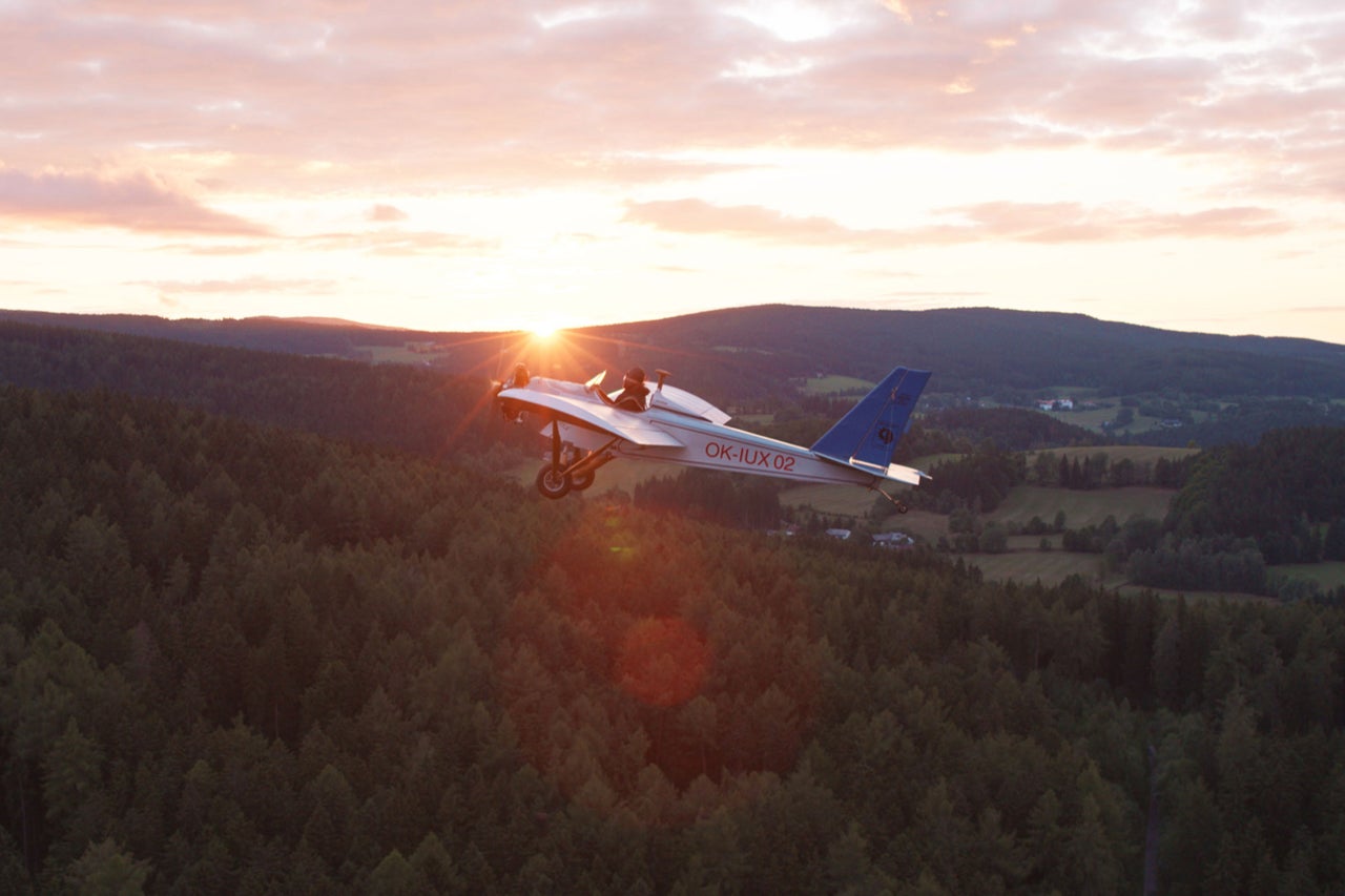 Kleinflugzeug fliegt über Wald bei Sonnenuntergang