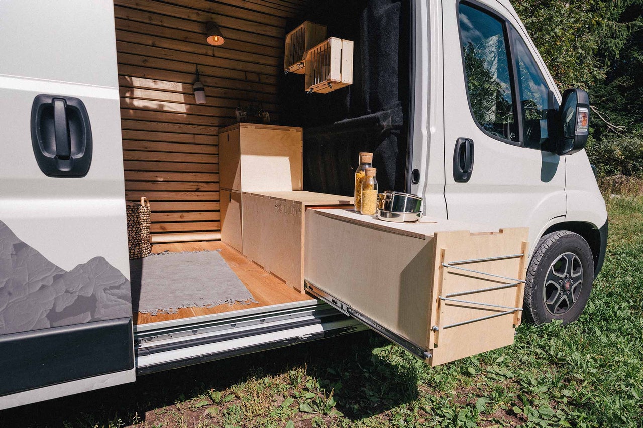 Innenraum eines Camper Vans mit Holzverkleidung, Küchenauszug und Vorräten