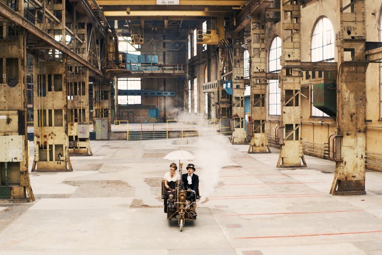 Zwei Personen fahren mit einem selbstgebauten Fahrzeug durch eine alte Fabrikhalle.
