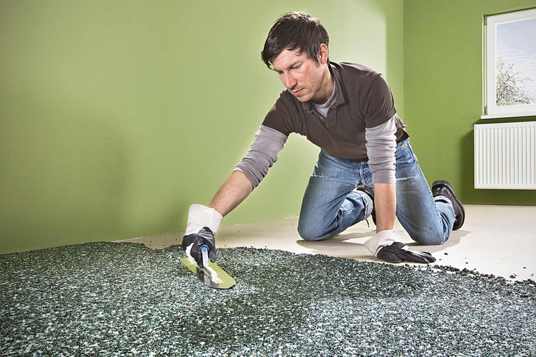Ein Mann verlegt einen Steinteppich mit einer Glättkelle in einem Raum.