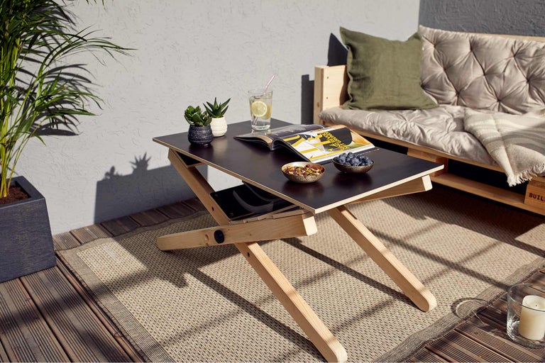 Szene im Außenbereich mit einem Holztisch, Snacks, Getränken und einem Palettensofa auf einem Teppich