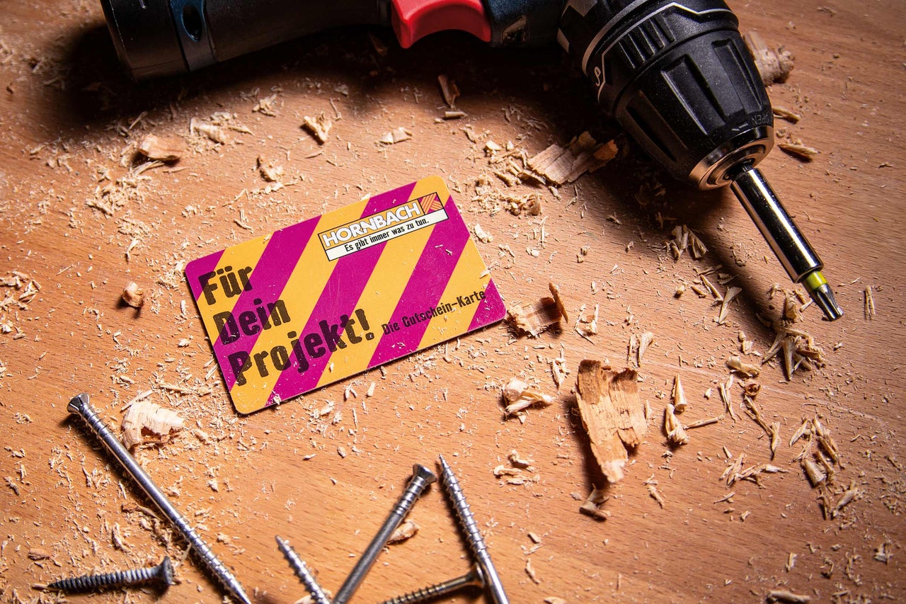 Szene mit einem Hornbach Gutschein, einem Akkuschrauber und Schrauben auf einer Holzoberfläche mit Holzspänen