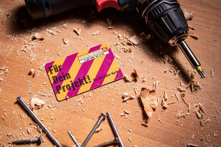 Szene mit einem Hornbach Gutschein, einem Akkuschrauber und Schrauben auf einer Holzoberfläche mit Holzspänen