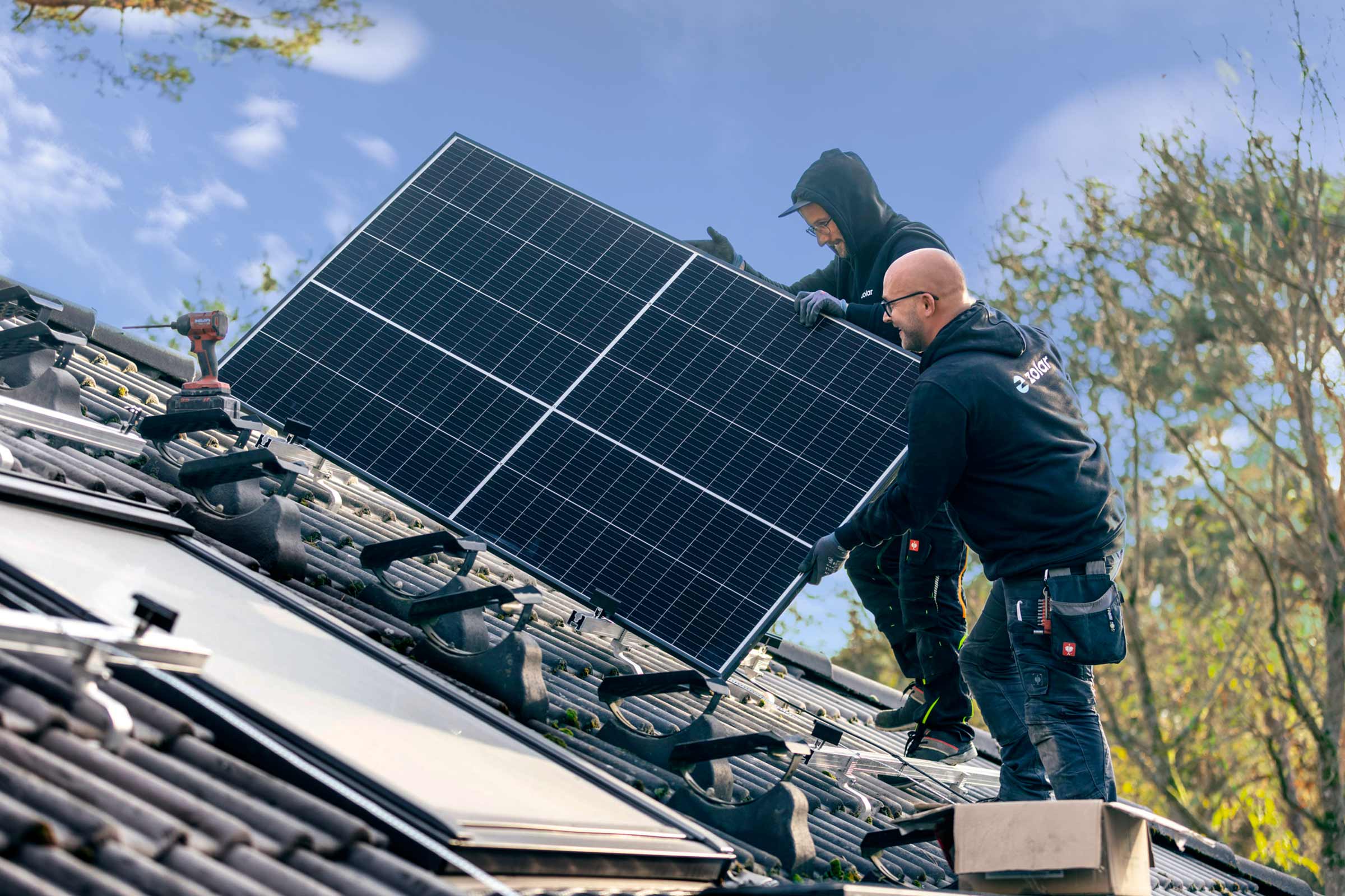 Zwei Handwerker montieren ein Solarmodul auf einem Dach zur Stromerzeugung.