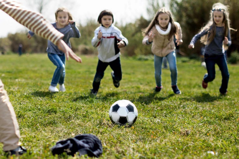Kinder spielen Fußball auf einer Wiese.
