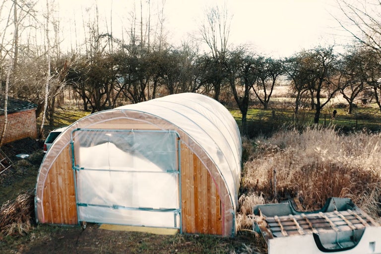 Gewächshaus mit Holzrahmen und transparenter Folie im Garten.