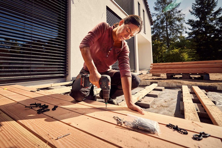 Frau montiert eine Holzterrasse mit einem Akku-Bohrschrauber.