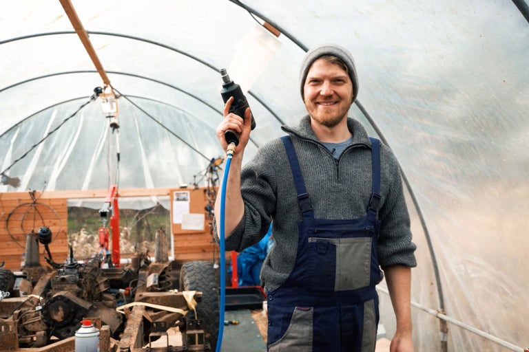 Mann hält Druckluftpistole in Werkstatt mit Fahrzeugteilen