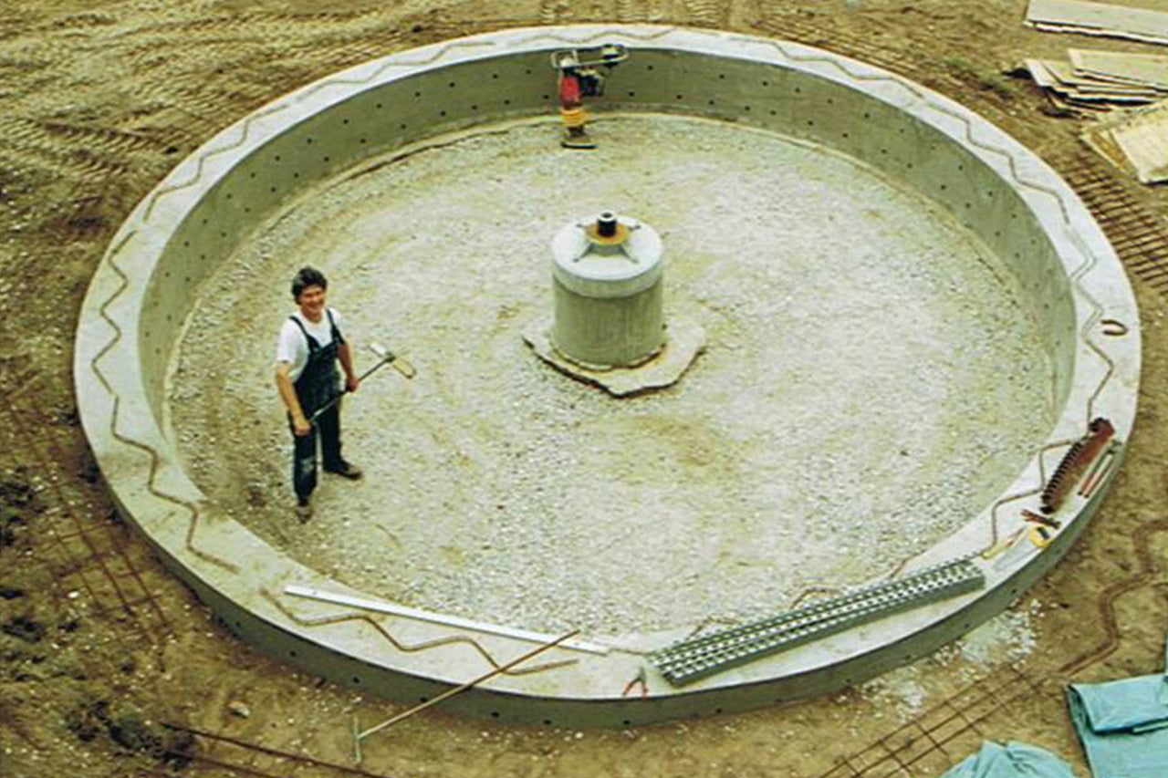 Baustelle mit rundem Betonfundament, Person und Baugeräten.