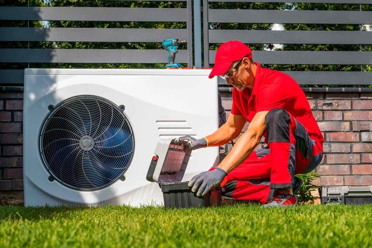 Ein Techniker wartet eine Wärmepumpe im Garten mit Werkzeugkasten