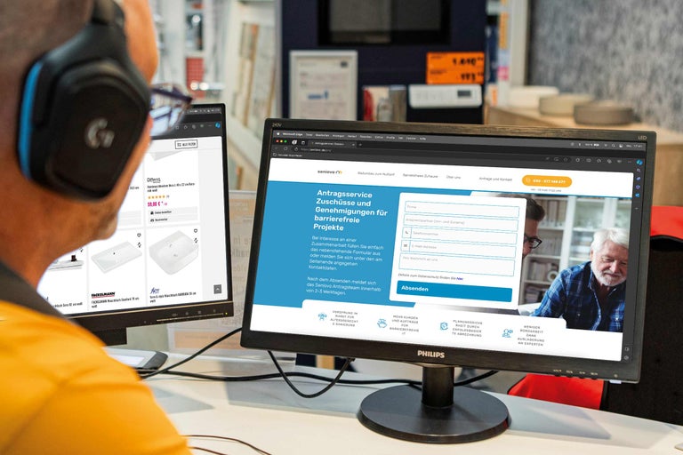 Person mit Headset vor zwei Computermonitoren. Auf dem linken Bildschirm ist die Hornbach Webseite zu sehen. Auf dem rechten Bildschirm ist die Webseite von Senovo zu sehen.