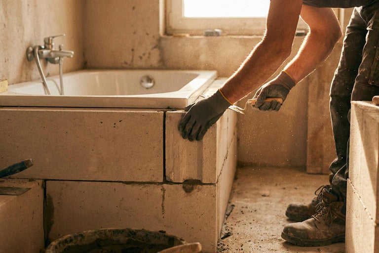 Ein Mann mauert eine Badewanne mit Porenbetonsteinen.
