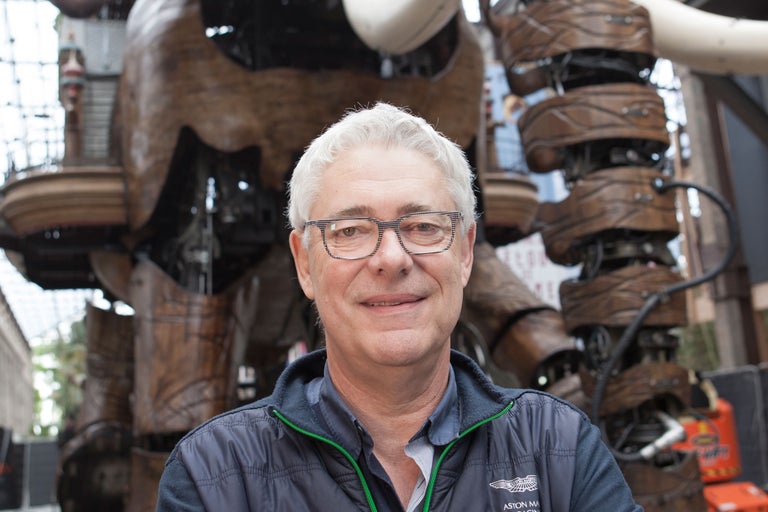 Porträt eines Mannes mit Brille vor einer hölzernen mechanischen Skulptur